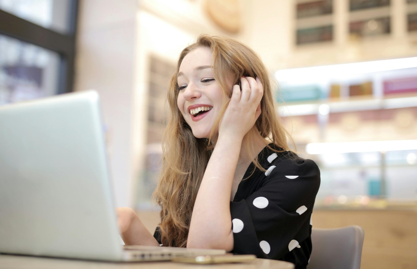 A cheerful woman engaged with her laptop in a cozy indoor setting.